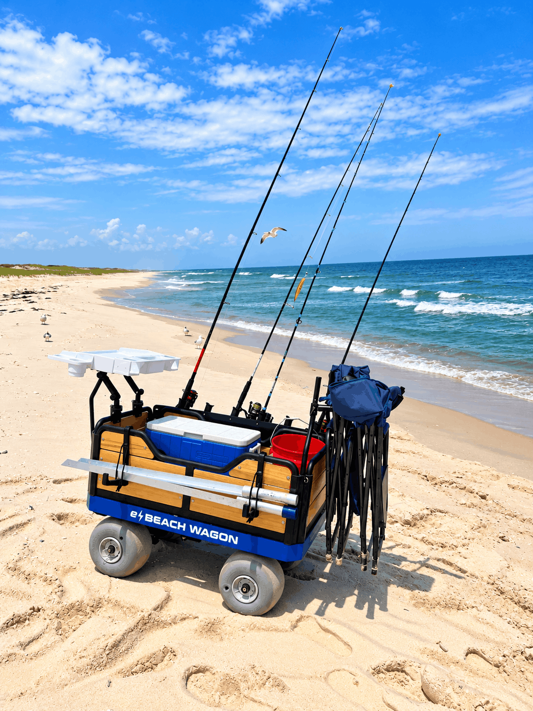 e-beach wagon at the beach, fully loaded with fishing gear: sand spike holders, fishing rod rack holders, fillet board. Electric motorized beach wagon for fishing enthusiasts