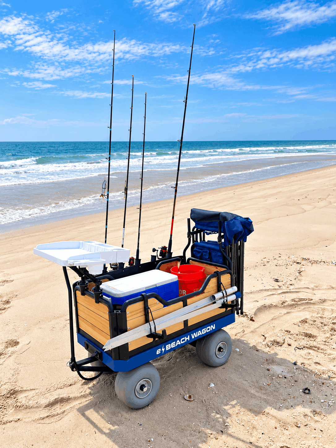 A powered electric beach cart, e-Beach Wagon, equipped with four fishing rods, a cooler, a red bucket, fillet board, and sand spike holders